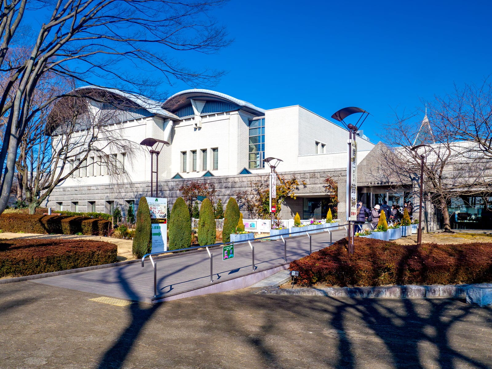 The white JRA Racing Museum building and its approach path under a clear winter sky.