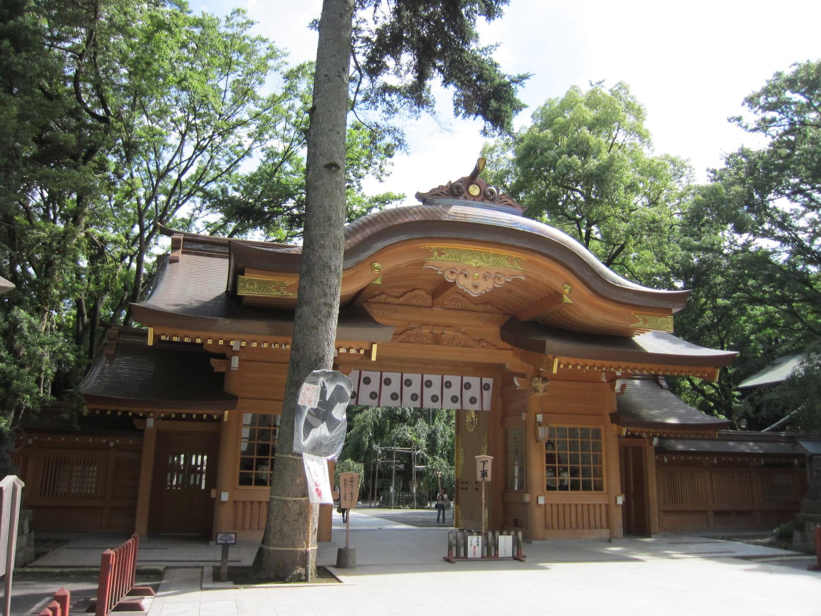 The wooden Zuishinmon gate of Okunitama Shrine with its curved copper roof, surrounded by trees.