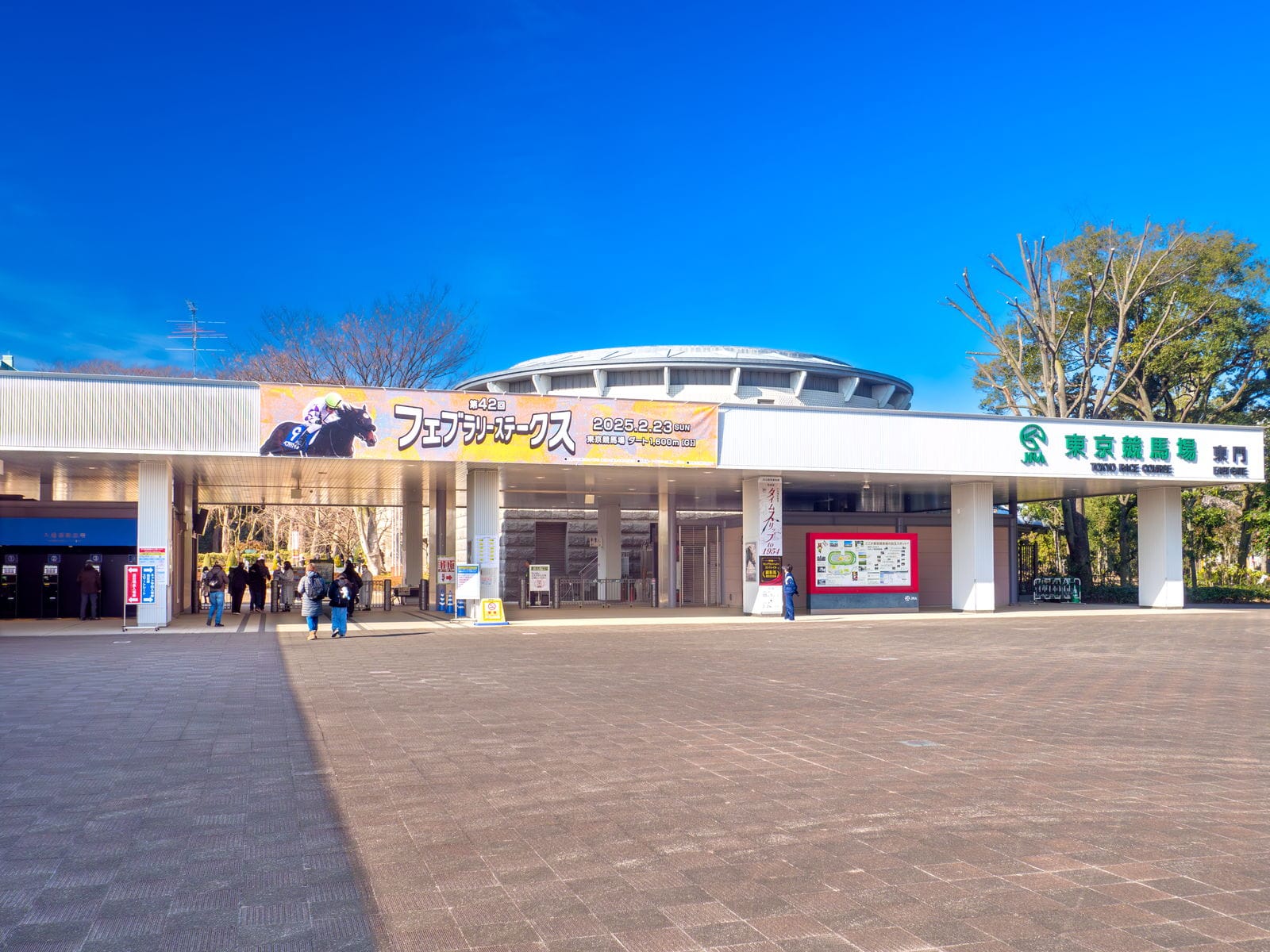 The East Gate of Tokyo Racecourse with its race banner, seen across the wide paved plaza.