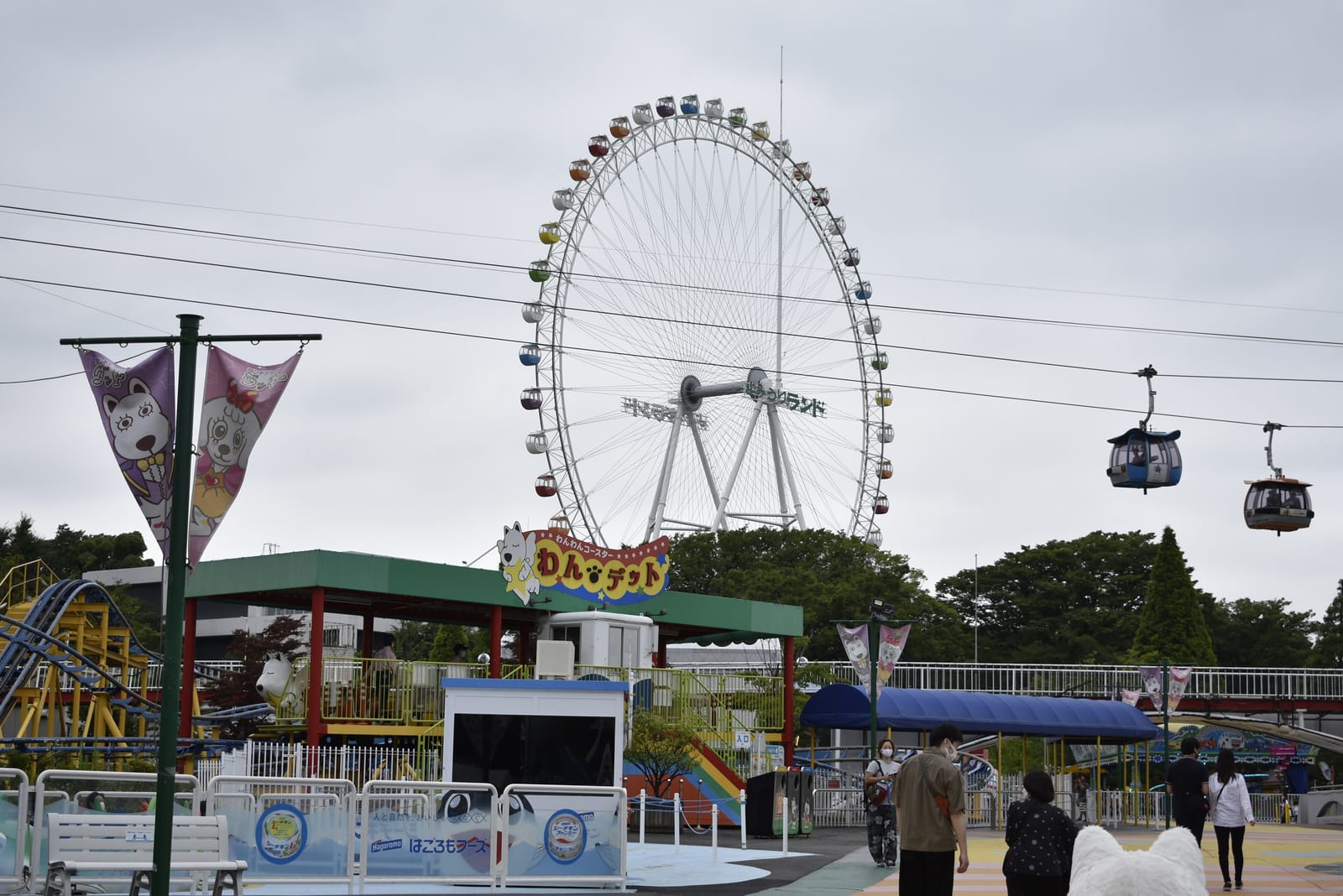 Yomiuriland's giant Ferris wheel with Sky Shuttle gondola cabins passing overhead on a cloudy day.