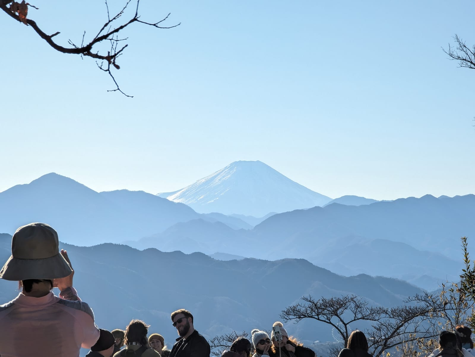 Hikers on the Mt. Takao summit looking west toward snow-capped Mt. Fuji on a winter morning.